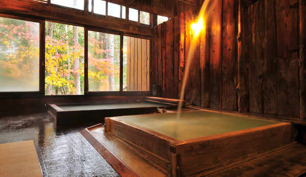 信玄の薬湯。打たせ湯のように注ぎ落ちた湯が、風情ある湯壺を青みがかった乳白色に変えながら満たします。