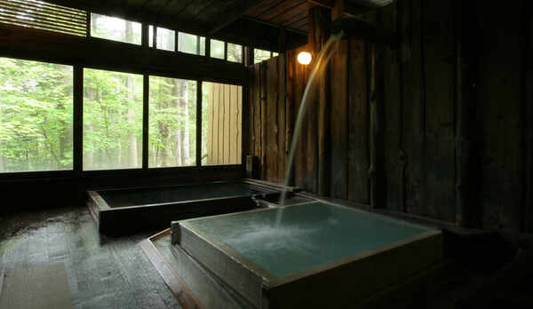 信玄の薬湯。打たせ湯のように注ぎ落ちた湯が、風情ある湯壺を青みがかった乳白色に変えながら満たします。