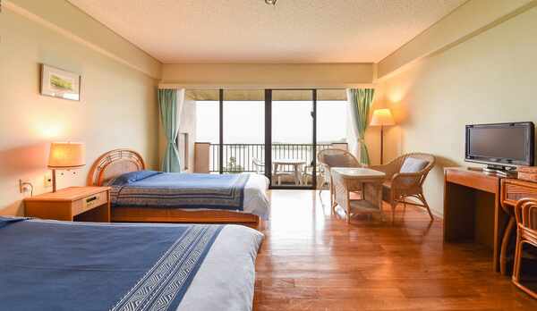 *［洋室ツイン］シングルベッドを配した客室。緑の芝とエメラルドグリーンの海が広がります。